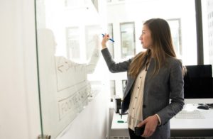 woman-wearing-gray-blazer-writing-on-dry-erase-board