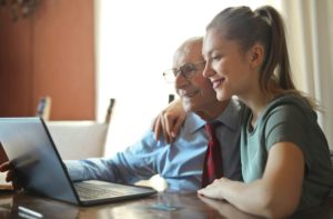 young-positive-woman-helping-senior-man-using-laptop