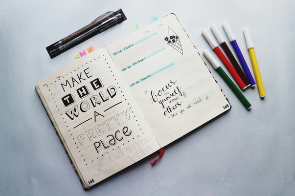 A-journal-with-the-quote-“make-the-world-a-pretty-place”-lying-on-a-neutral-table-with-stationary