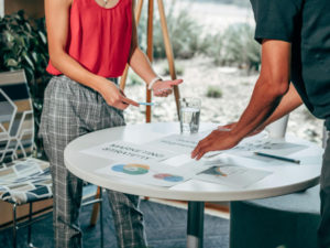 a-man-and-woman- are-positioned-around- a-table-filled- with-papers