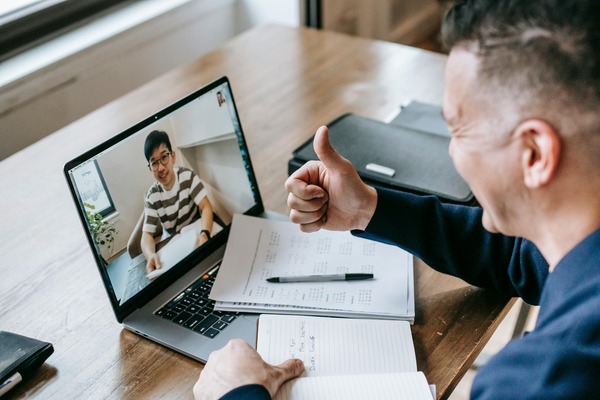 Two people having a video call, with one giving a thumbs-up and taking notes via online outsourcing