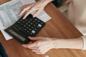 a-woman-sitting-on-a-chair-and-using-a-calculator-on-a-desk-beside-a-paper.