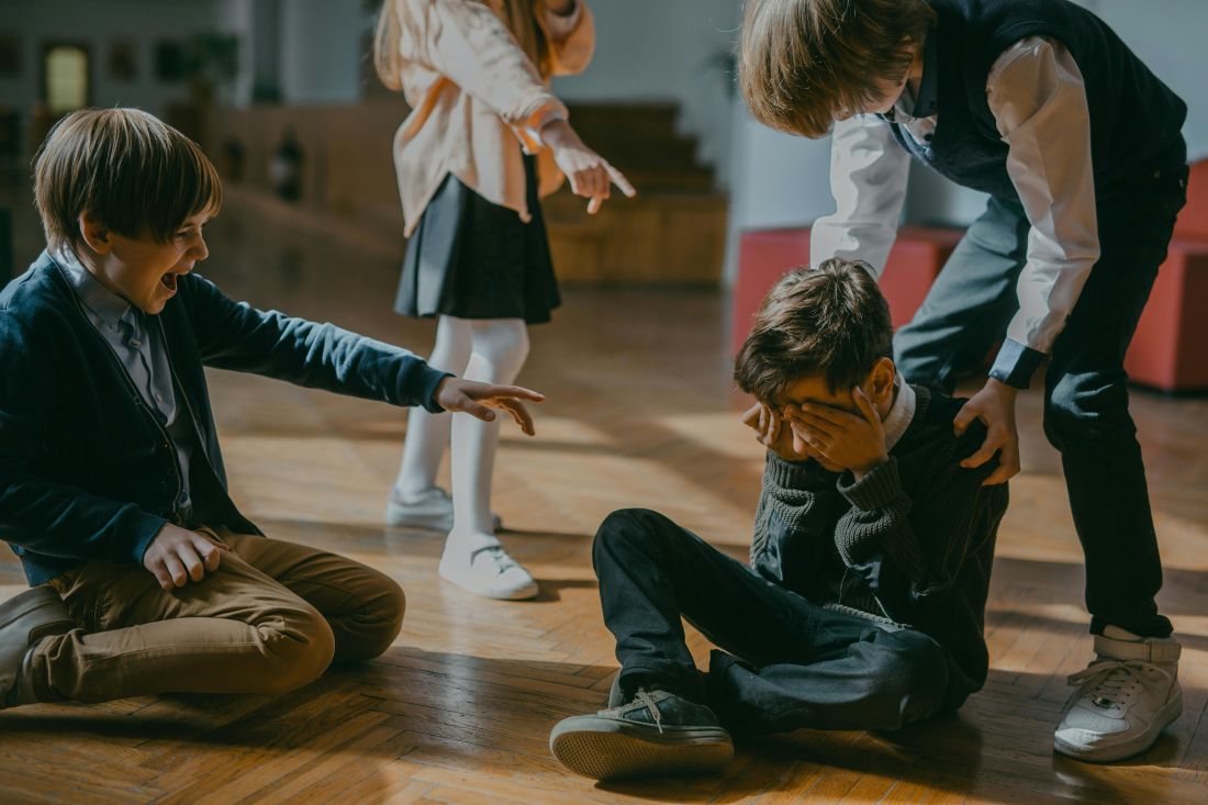 Three children bullying a child who is sitting on the floor