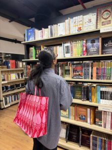 muqadsa-browses-through-shelves-lined-with-books-her-red-tote-bag-catches-the-light