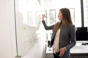 woman-wearing-gray-blazer-writing-on-dry-erase-board