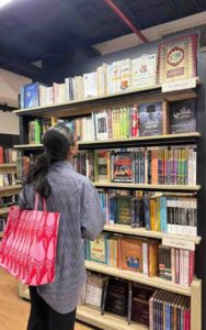 muqadsa-stands-in-front-of-a-bookshelf-shouldering-her-bag-which-is-bright-in-color