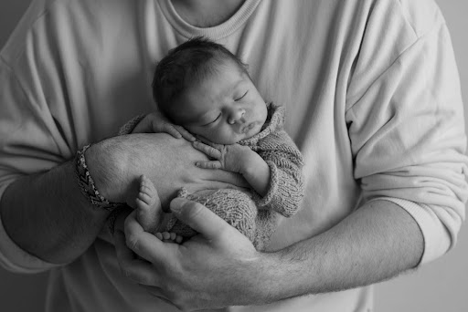 A newborn baby sleeping peacefully in a parent’s arms.