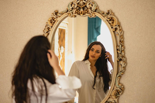Woman softly touching her hair while admiring her reflection in a vintage mirror.
