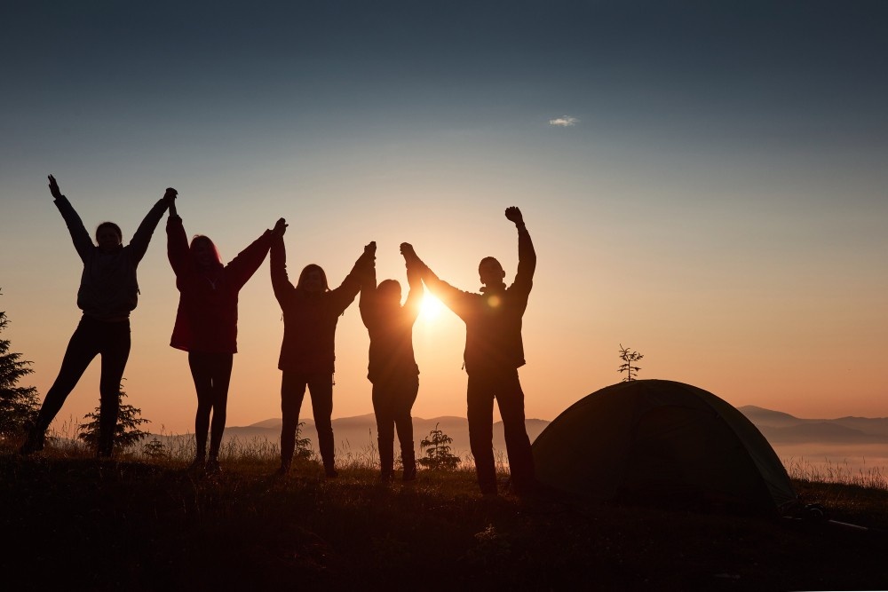 five-friends-camping-at-dusk-raising-their-hands-in-the-air