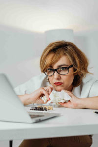 a-woman-intently-gazes-at-her-laptop-screen-with-a-chessboard-positioned-in-the-foreground-showcasing-her-focus-on-both-the-game-and-her-digital-workspace