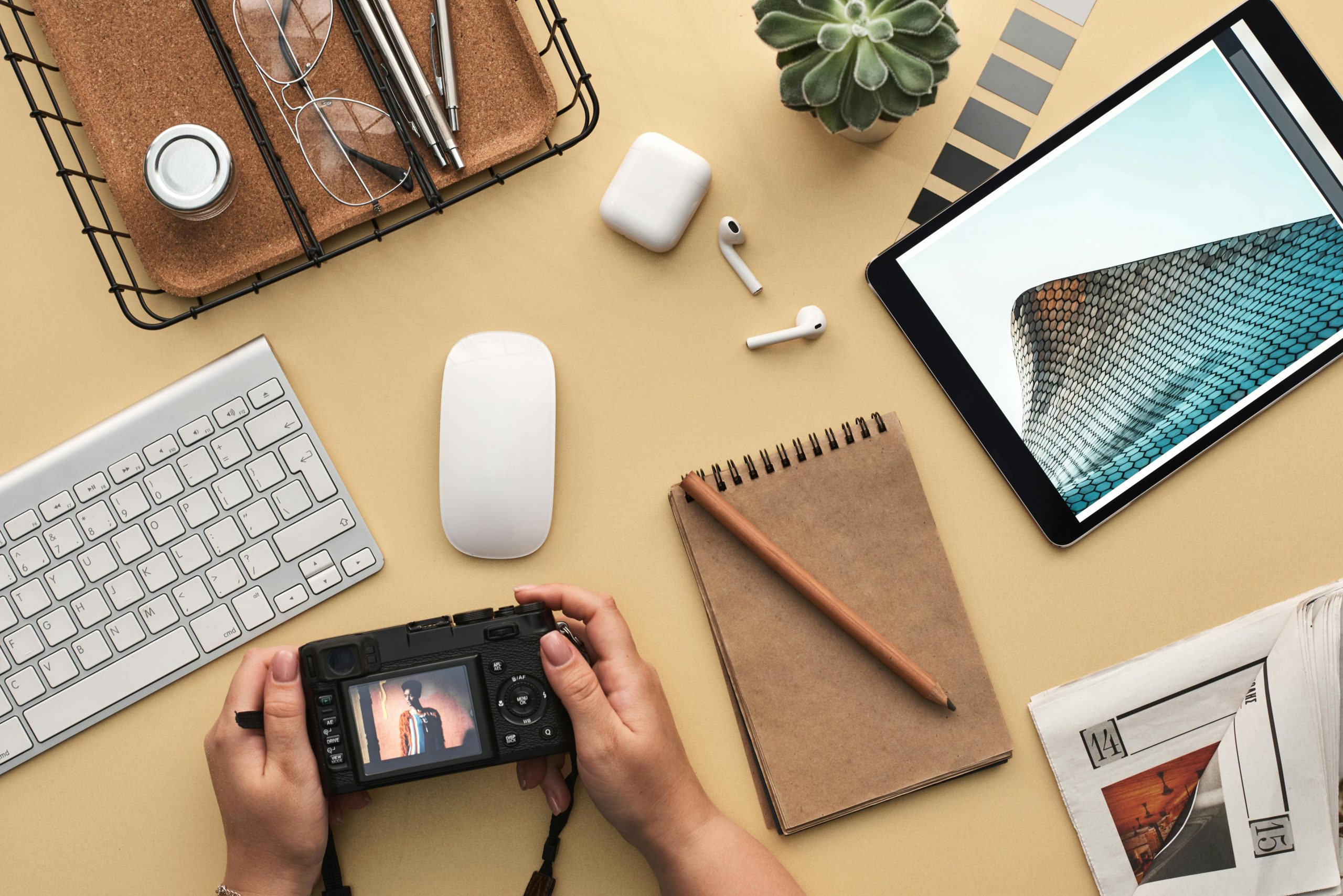 How to find your creativity tips person holding a camera on a work desk with items scattered such as tablet, notebook, pen and other