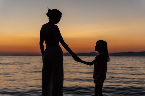 a-woman-and-child-holding-hands-at-sunset