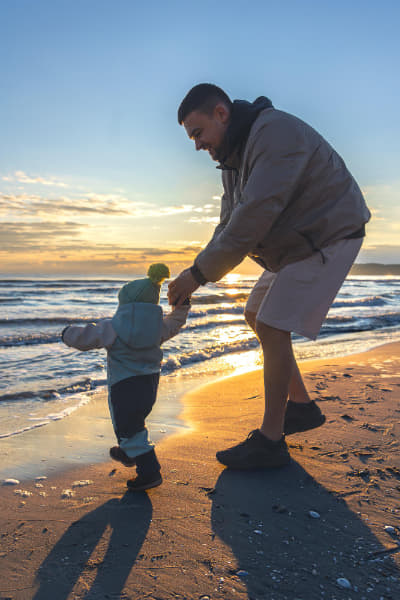 father-supports-child-sand-near-waves-sunset-toddlers-first-steps