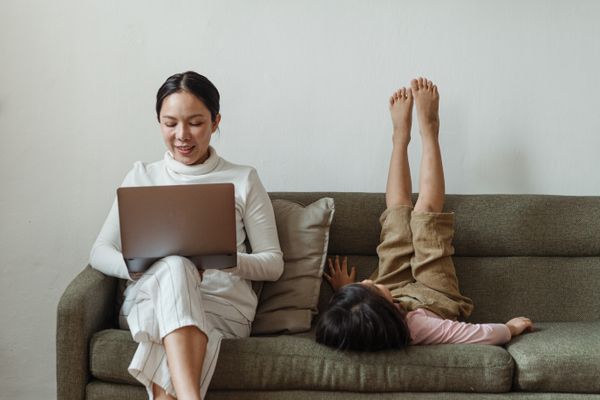 cheerful-mother-working-on-laptop-near-daughter-on-couch