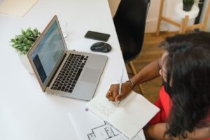 Person writing beside open laptop