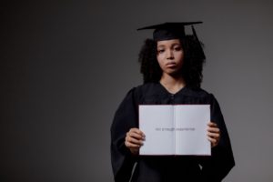A graduate looking sad, holding “Not Enough Experience