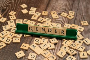 Wooden letter tiles spelling “GENDER” on a table surrounded by scattered letters.