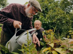An adult and a child tending a plant together in a garden