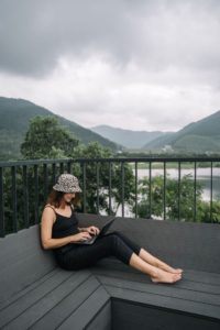 Woman working remotely with laptop on a terrace surrounded by scenic mountains and lake view. 
