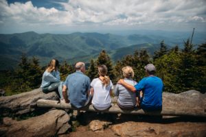 Five family members sitting on a log bench facing a mountain view