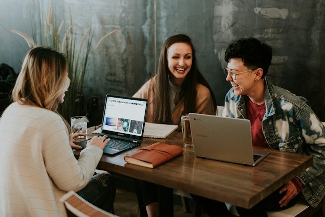 three people sitting together in front of a table laughing. 