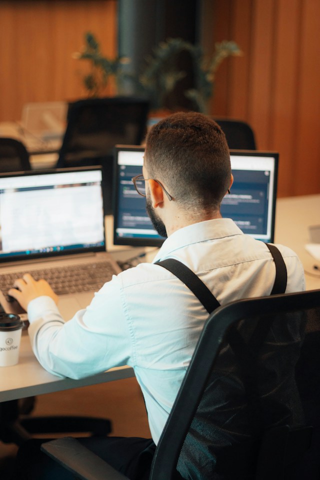 a man sitting at a desk with two laptops.